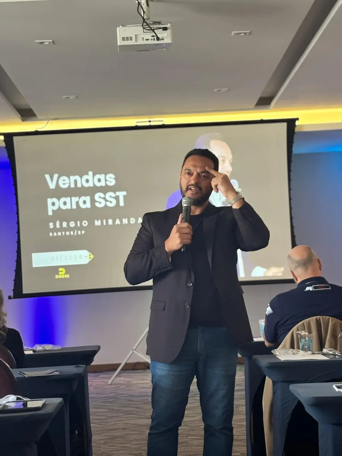 Sérgio Miranda apresentando o slide “Vendas para SST” no palco.