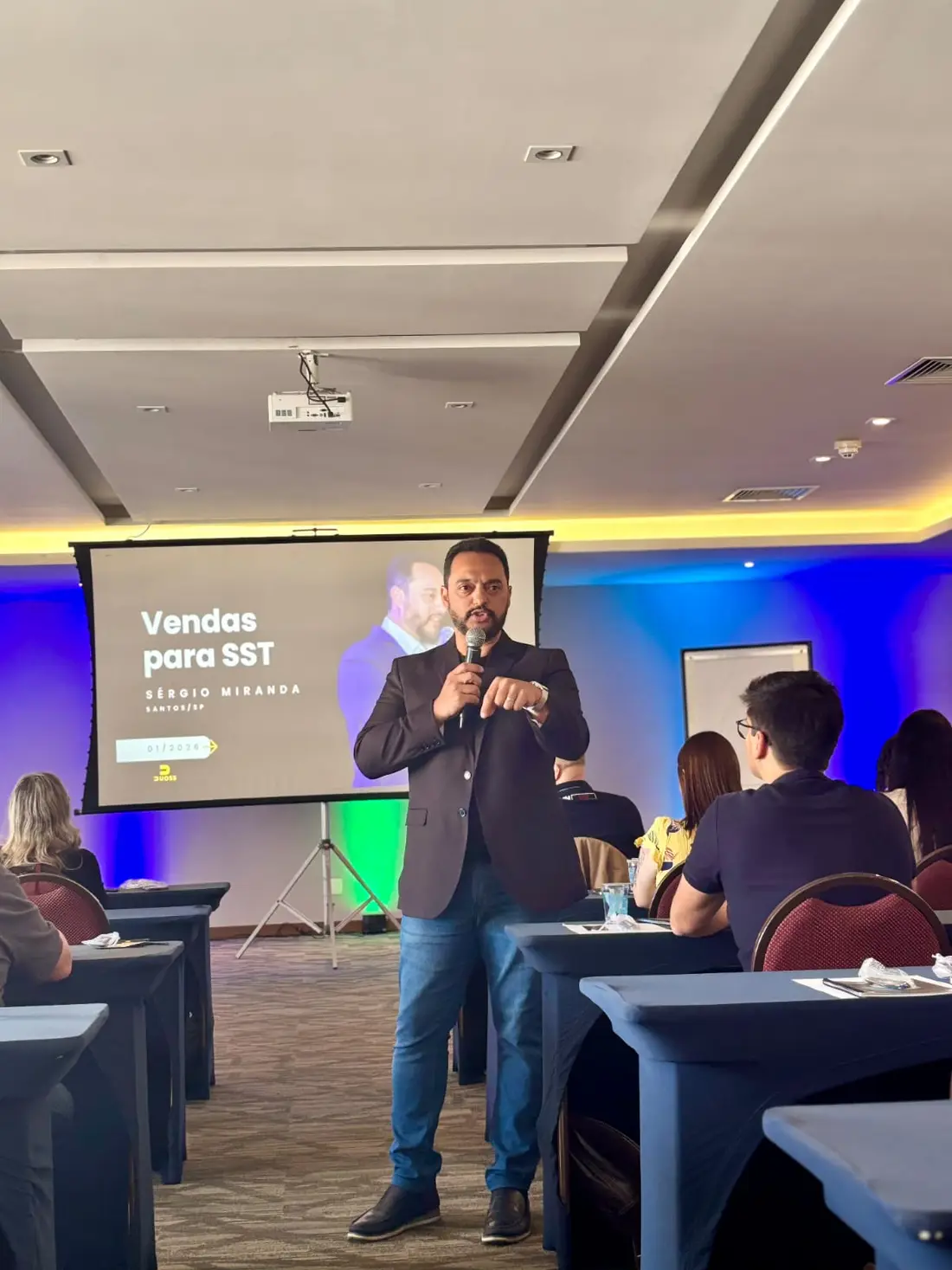 Participantes assistindo à apresentação sentados nas mesas.