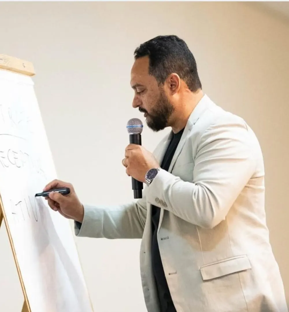 Sérgio Miranda conduzindo o 1º Treinamento de Vendas para SST, escrevendo em um flip chart com microfone na mão.